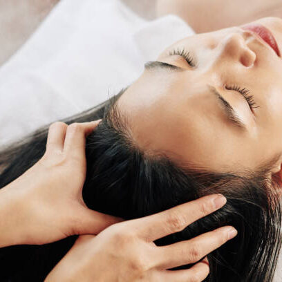 Close-up image of beautician massaging head of female client relaxing on massage bed